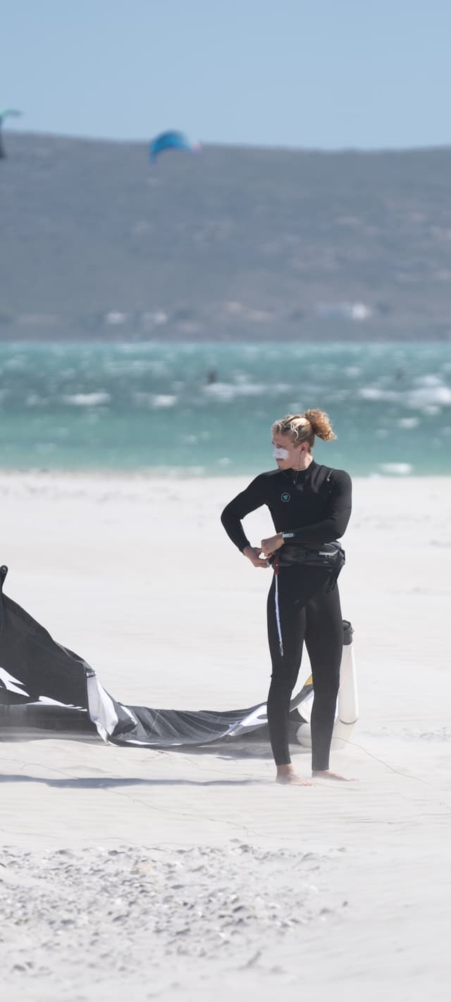 Anton Billstein, Kitelehrer und Mitgründer von Reise ins Blaue, im Neoprenanzug am Strand beim Aufbauen seines Kites