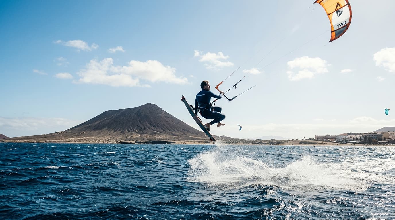 Kitesurfer in der Bucht von El Médano auf Teneriffa vor der Kulisse des Montaña Roja bei sonnigen Passatwind-Bedingungen.