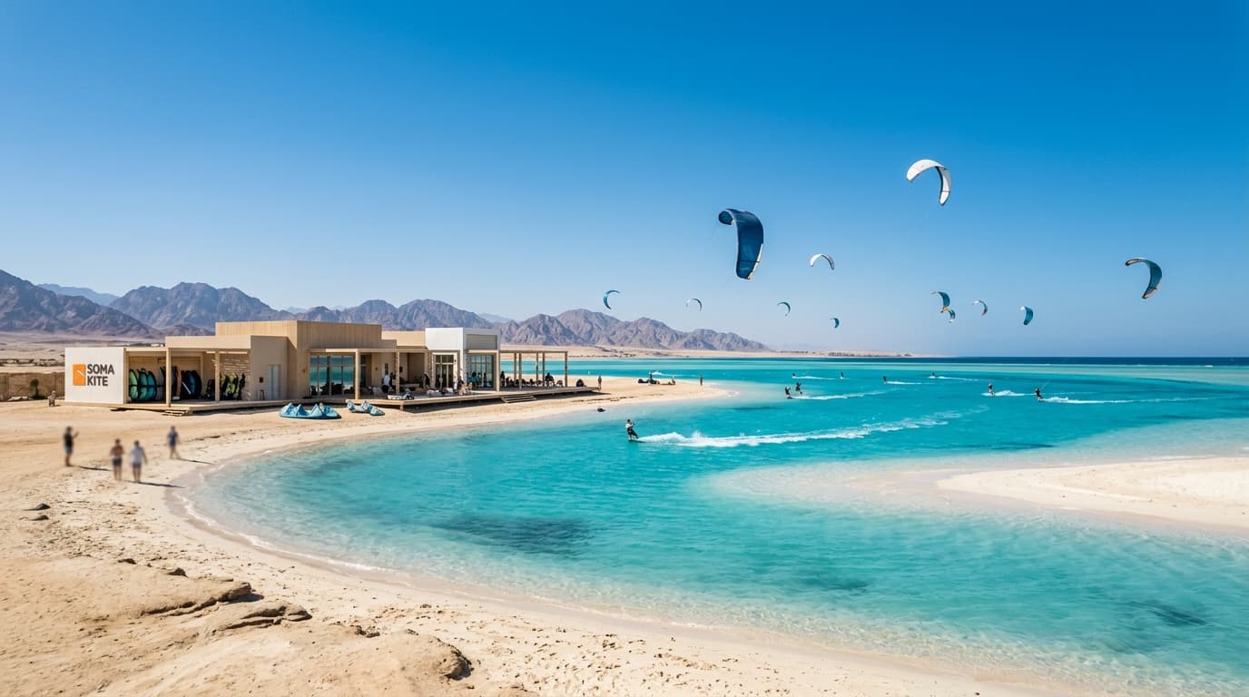 Blick auf die türkisfarbene Lagune der Soma Bay in Ägypten mit Kitesurfern auf dem Wasser vor einer modernen Kiteschule unter blauem Himmel.